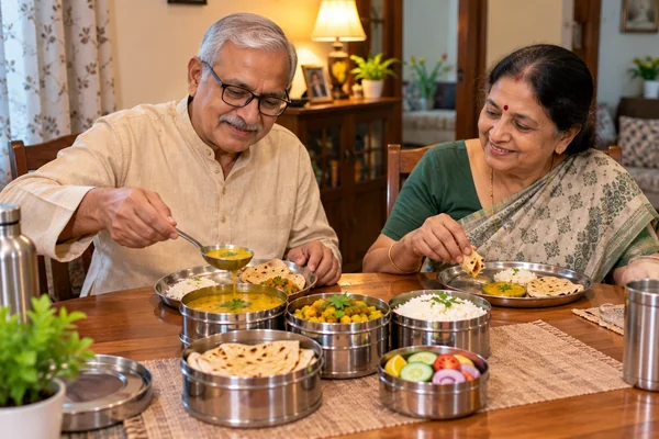 Elderly couple sharing a light home-style dinner tiffin at their table in South TT Nagar, Bhopal